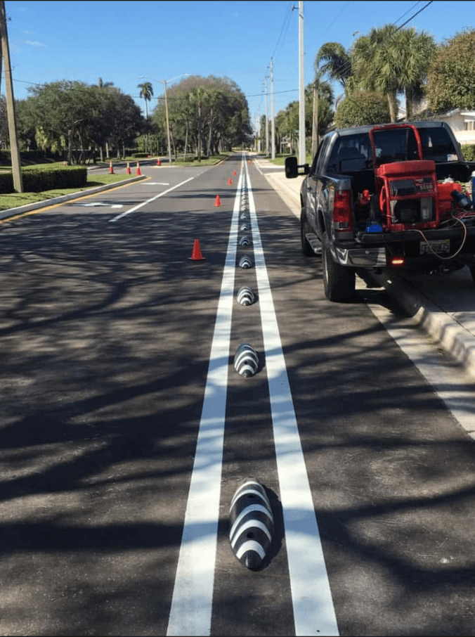 Freshly painted lane lines with reflective lane delineators down a Florida residential road, with the Trinity Striping work truck in view