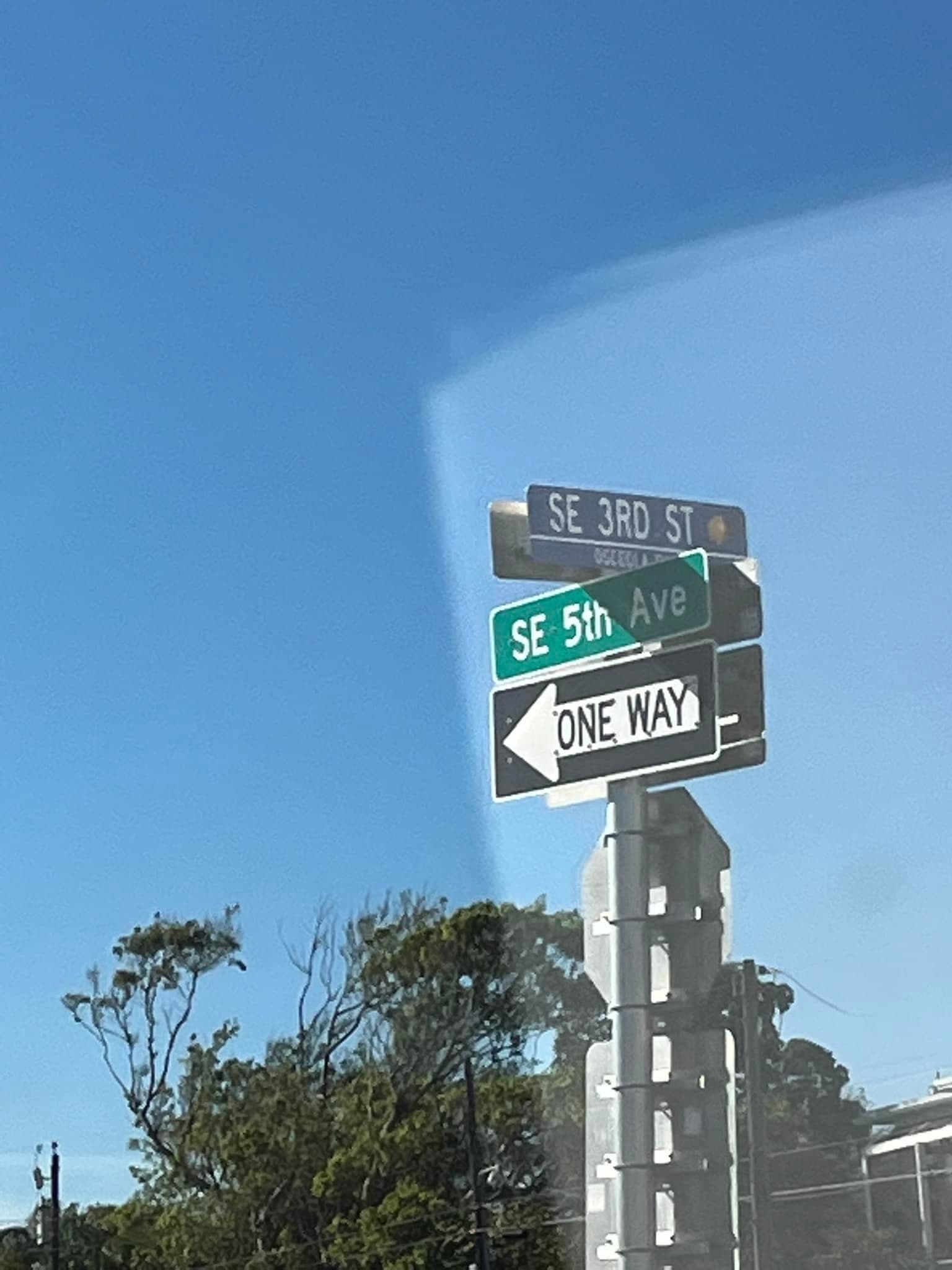 Newly installed street name and one-way signs mounted on a pole against a blue Florida sky